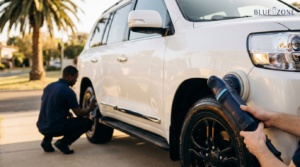 Mechanic kneels by a white SUV, removing the front wheel with a power tool in hand