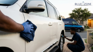 Technician wiping a white SUV with a blue cloth during a car detailing service, Bluezone van in background.